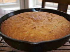 a baked cake in a black pan on a wire rack next to a wooden table