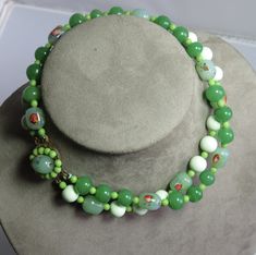 Here's a vintage green art glass bead choker necklace from the mid century.  It features an assortment of jade green glass beads, some of which have embedded color swirls.  Beads are all in nice condition, and necklace measures 14" long with a decorative box clasp.  Can easily be made into a single long strand.  Matching clip earrings will be included, but they are not in good condition.  Please see the image with the coin for a size comparison as images often appear larger than actual size. This is necessary to provide accurate details.   Thanks for looking. Green Glass Round Bead Jewelry, Vintage Green Glass Beaded Necklaces, Green Vintage Glass Beaded Necklaces, Green Large Beaded Glass Necklaces, Green Glass Beaded Necklace With Large Beads, Vintage Jade Beaded Necklaces, Green Glass Round Bead Necklaces, Green Glass Round Beads Necklaces, Green Czech Glass Necklaces With Large Beads