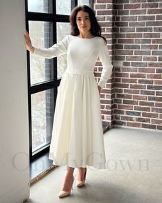 a woman standing in front of a window wearing a white dress