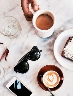 a table topped with two cups of coffee next to a plate of cake and a cell phone