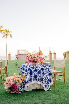 a table with flowers on it in the middle of some grass next to two chairs