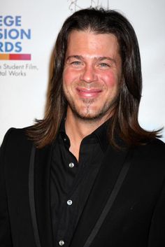 a man with long hair wearing a black suit