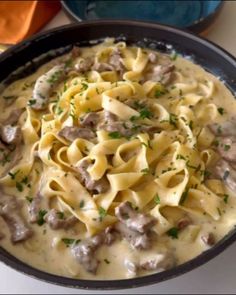 a skillet filled with pasta, meat and sauce on top of a white table