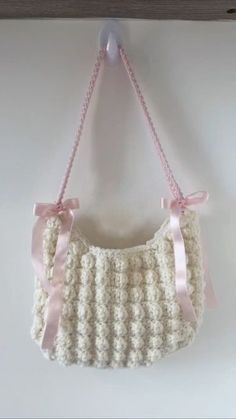 a crocheted purse hanging on a wall with pink ribbon around the handles and bottom