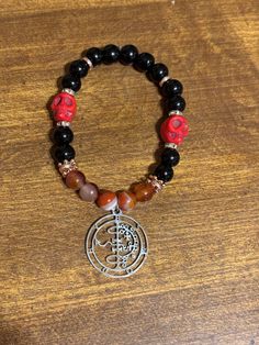 a bracelet with a silver tree charm and red, black, and brown beaded beads