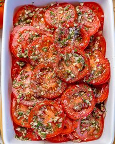 a white casserole dish filled with sliced tomatoes and seasoning sprinkles