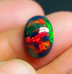 a close up of a person's hand holding a ring with an orange and green design on it