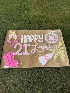 a cardboard sign that says happy 21st birthday on the grass in front of some flowers