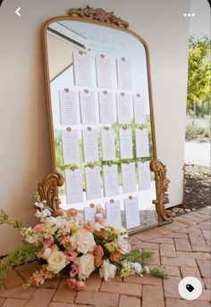 a table with flowers and a mirror on the ground next to it that has a seating chart in front of it