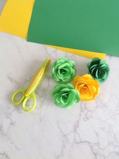 paper flowers and scissors on a marble countertop with green, yellow, and orange cards