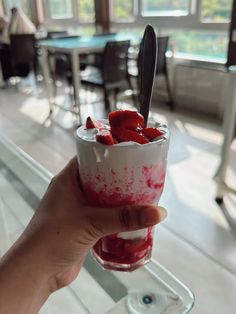 a person holding up a small glass with strawberries in it and ice cream on top