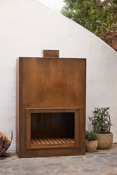 a fire place sitting on top of a stone floor next to potted plants and a white wall