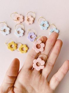 a hand holding several different colored earrings on it's fingers, with flowers in the middle