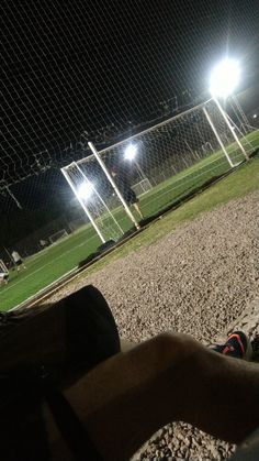 a person laying on the ground in front of a soccer field at night with lights