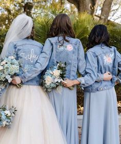 three bridesmaids in light blue dresses and denim jackets with embroidered words on them