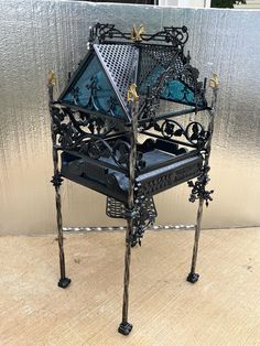 an iron and glass bird feeder sitting on top of a wooden table next to a wall