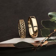 two gold wedding rings sitting on top of a wooden table next to leaves and flowers