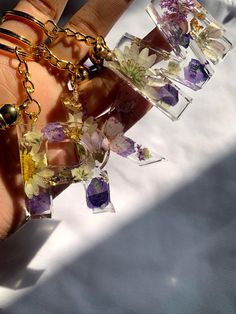 a person's hand is holding several small glass pieces with flowers in them and gold chains