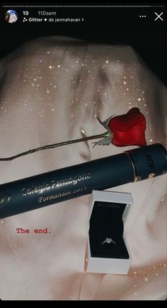 a red rose sitting on top of a white shirt next to a black pen and ring