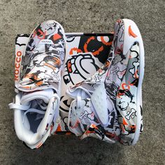 a pair of white shoes with orange and black designs on them sitting on the ground