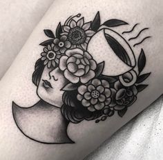 a woman's head with flowers and crescent tattoo on her thigh, done in black ink