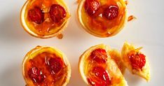 four small pastries with jam on them sitting on a white surface, ready to be eaten