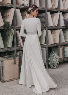 a woman standing in front of a book shelf wearing a white dress and flower in her hair