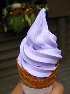 a hand holding an ice cream cone with purple icing on it's top