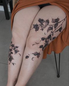 a woman sitting on a chair with her legs covered in flowers and leaves tattooed on her leg