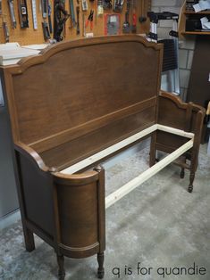 a wooden bed frame sitting on top of a floor next to a wall filled with tools