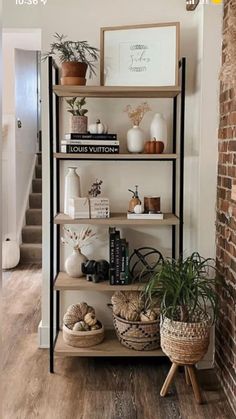 a shelf filled with books and plants in front of a brick wall next to a stair case