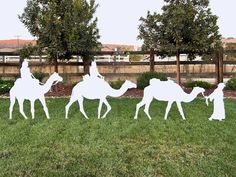 three white paper cut out of people riding camels in the grass with trees behind them