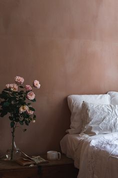 a bed with white linens and pink flowers in a vase on the side table