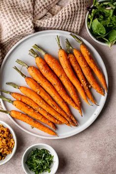 a white plate topped with lots of carrots next to bowls filled with greens and seasonings