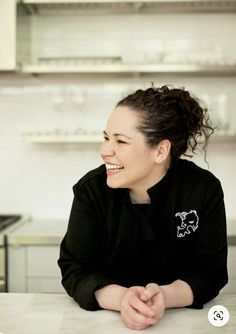 a smiling woman sitting at a counter in a kitchen