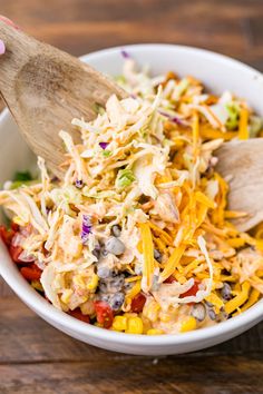 a person holding a wooden spoon in a bowl filled with coleslaw and beans