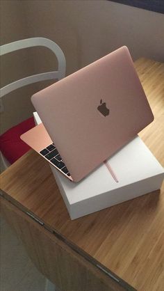 an apple laptop sitting on top of a white box next to a wooden table with a red chair