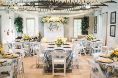 a dining room with tables and chairs covered in blue and white cloths, decorated with yellow flowers