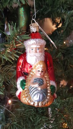 a christmas ornament hanging from a tree with santa holding a baby's head