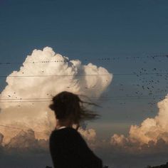 a woman standing in front of a large cloud with birds flying above her and the sky behind her