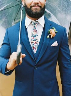 a man in a suit holding an umbrella and smiling at the camera while wearing a flowered boutonniere