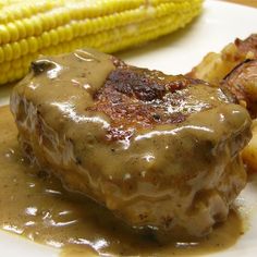 a white plate topped with meat covered in gravy next to corn on the cob