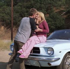 a man and woman kissing on the hood of a car