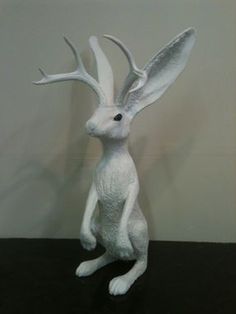 a white sculpture of a rabbit sitting on top of a black table next to a wall