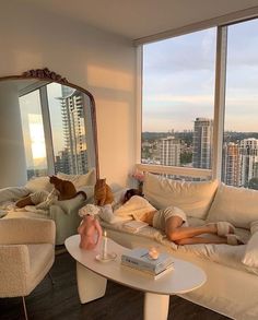 a man laying on top of a white couch next to a window in a living room