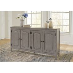 a gray sideboard sitting on top of a rug in front of a large window