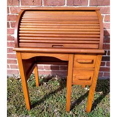 a wooden desk sitting in the grass next to a brick wall on top of green grass