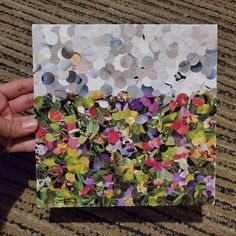 a hand holding up a piece of paper with flowers on it and confetti