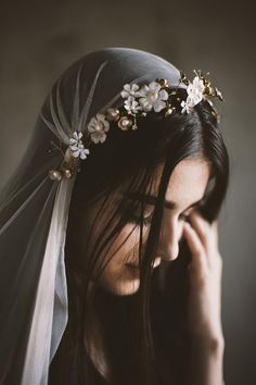 a woman wearing a veil with flowers on it's head and holding her hand to her face