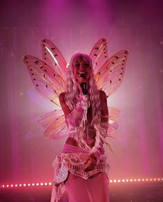 a woman dressed as a fairy holding a microphone in front of a stage with lights